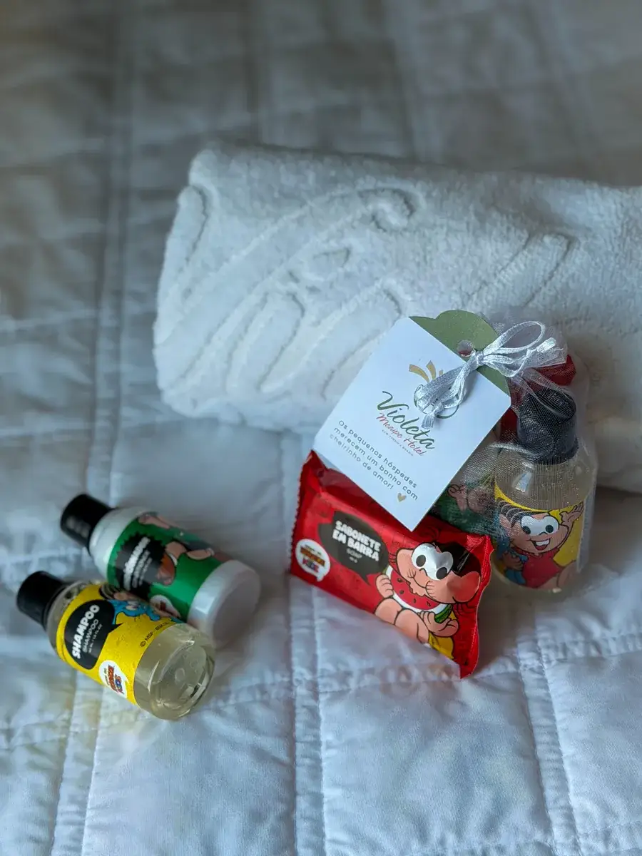 Kit infantil da Turma da Mônica, com xampu, condicionador, sabonete e cartão do hotel, ao lado de uma toalha enrolada