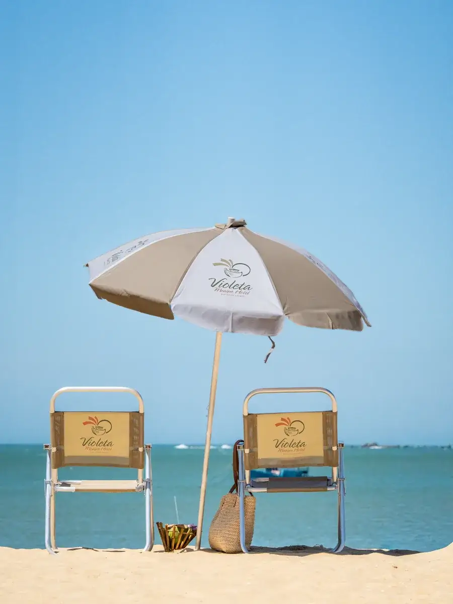 Guarda-sol e duas cadeiras com a marca do hotel na areia de Meaípe, de frente para o mar