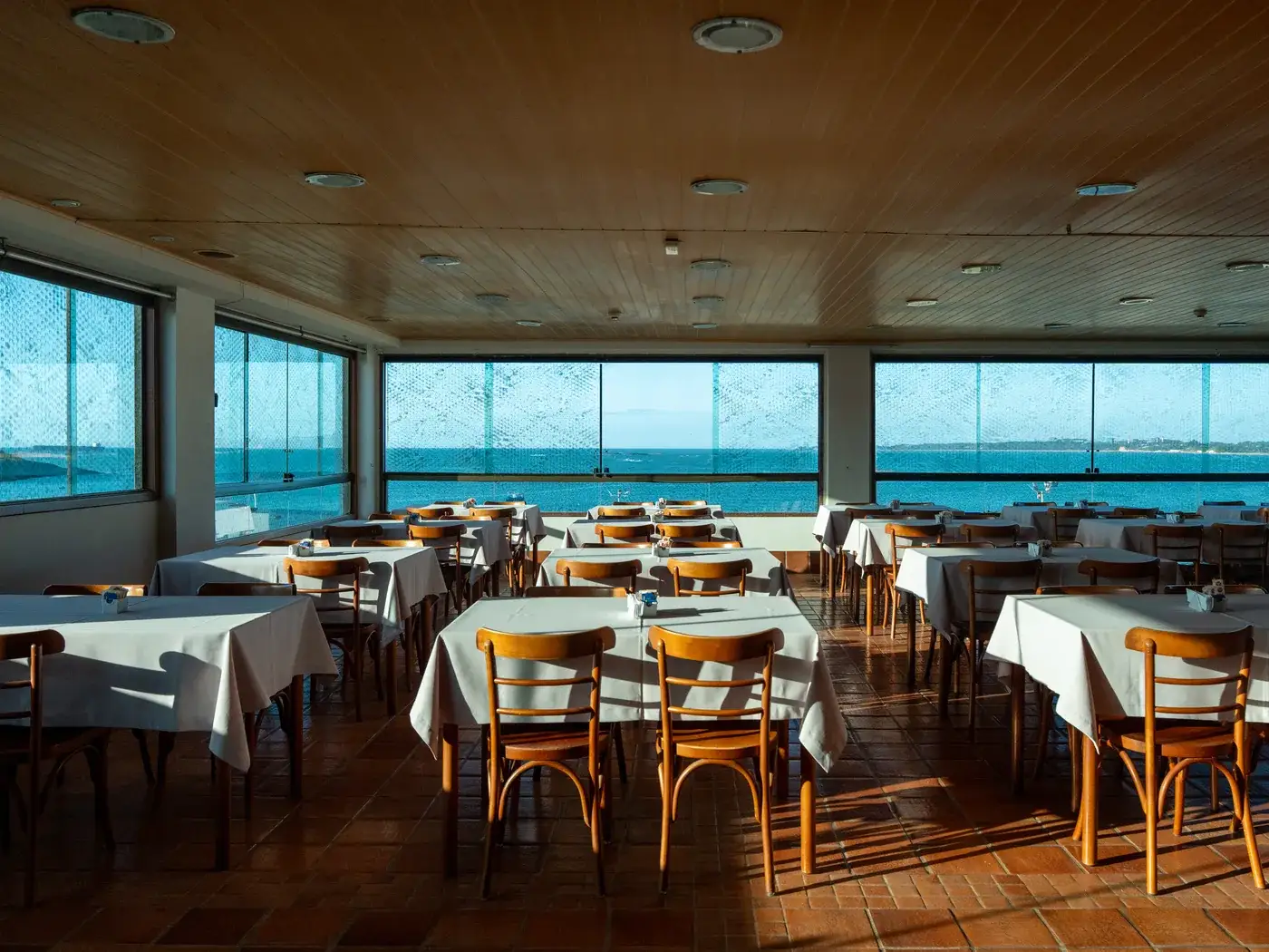 Salão do café da manhã com as mesas postas e o mar nas janelas panorâmicas