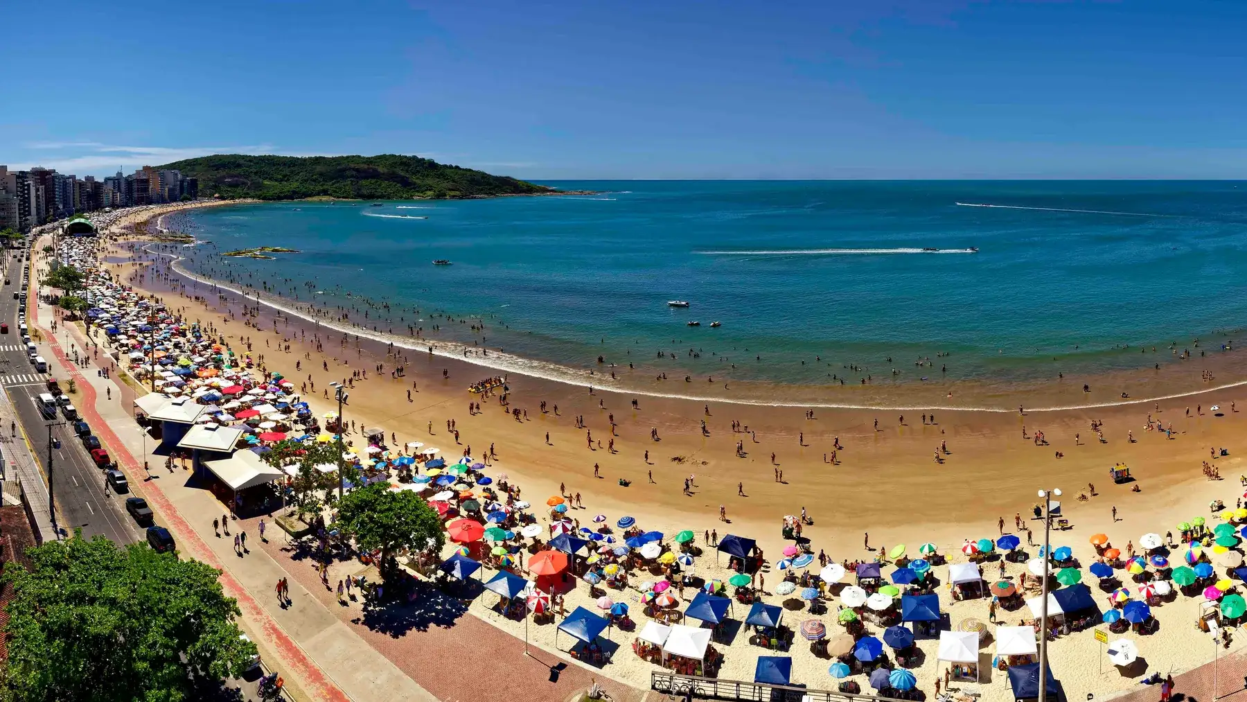 Vista alta da curva inteira da Praia do Morro, com o calçadão e as barracas enfileiradas na areia