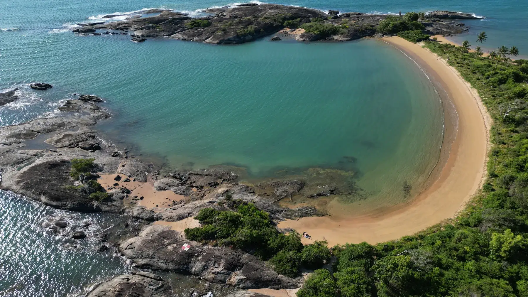 Uma das Três Praias vista de drone, com a faixa de areia em meia-lua entre os rochedos e a mata