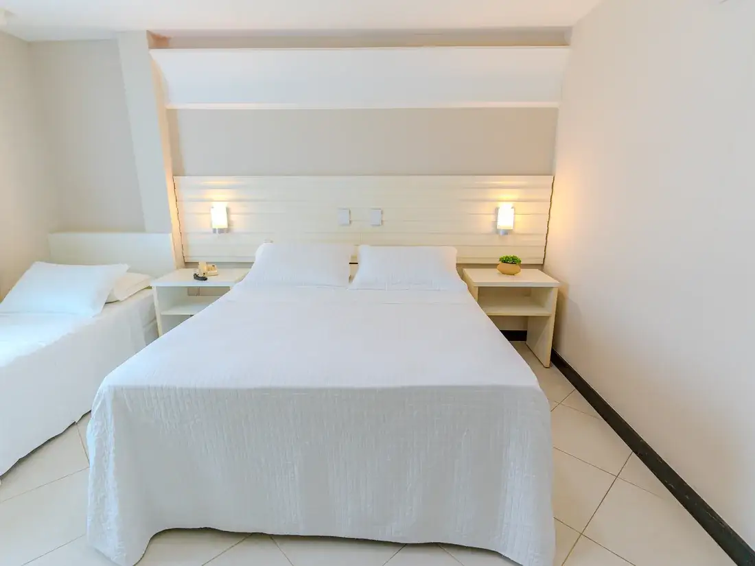 Cama queen vista de frente, com luminárias de cabeceira e a cama de solteiro ao lado